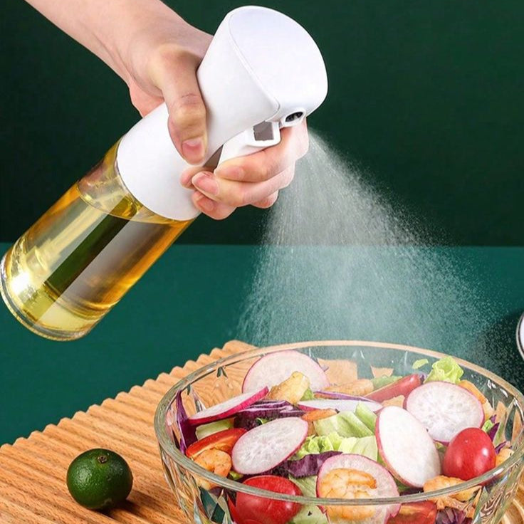 Person using a oil sprayer over a salad on a wooden board with a green background