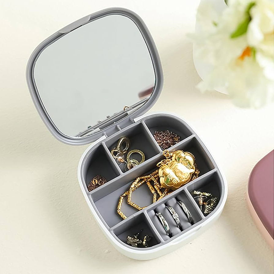 Jewelry organizer with compartments containing gold and silver jewelry on a light surface.