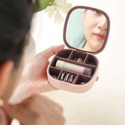 Compact pink jewelry case with mirror held by a person, containing lip balm, earrings, and other small items.