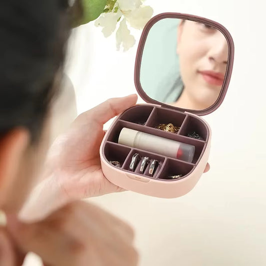 Compact pink jewelry case with mirror held by a person, containing lip balm, earrings, and other small items.