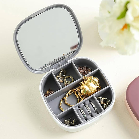 Jewelry organizer with compartments containing gold and silver jewelry on a light surface.